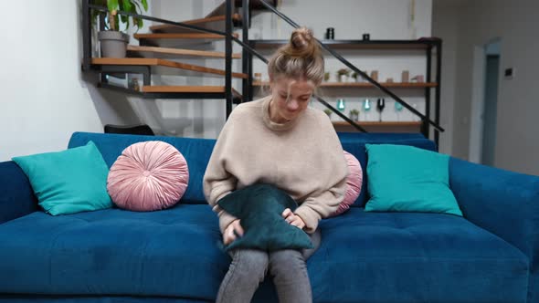 Angry Stressed Teenage Girl Hitting Cushion Sitting on Couch in Living Room at Home