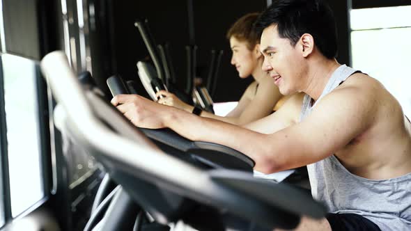 Attractive Asian Young Couple Riding on the Spinning Bike at the Gym Together