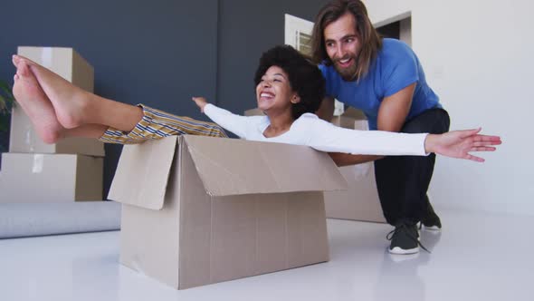 Caucasian man pushing his wife sitting in cardboard boxes at new apartment house