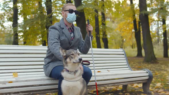 Blind Man Wearing Safety Man Sitting on Bench with Walking Stick and Guide Dog in Autumn Park