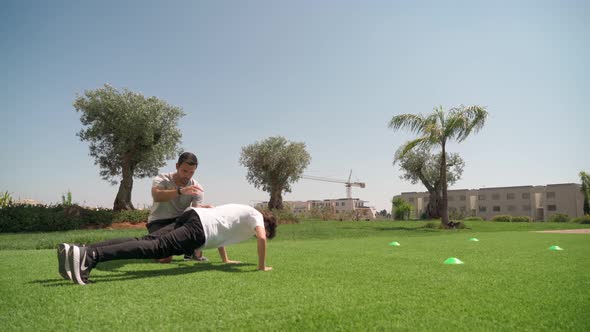 A Young Guy with a Personal Fitness Trainer Performs Pushups and Resistance Runs for Endurance and