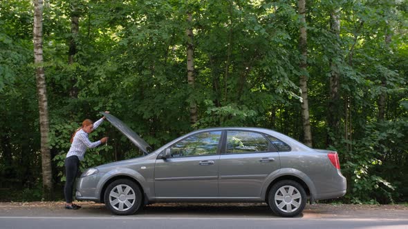 A Young Woman a Broken Car and Opens the Hood in the Forest. 