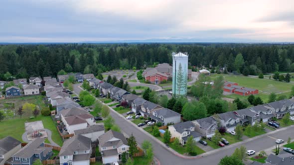 Orbiting aerial shot around a suburban water tower with a neighborhood in the foreground.