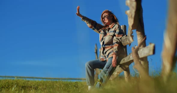 Young woman in meadow raising hand, shielding eyes from warm summer sun