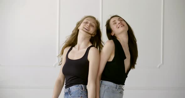 Two Slender Girls, One Blonde, the Other Brunette Posing for the Camera in the White Studio. They