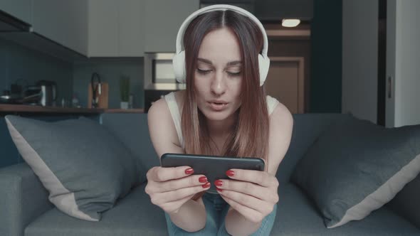 Female with Headphones Sitting with Plays a Smartphone