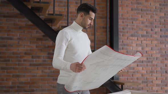Talented Handsome Middle Eastern Architect Examining Blueprint Standing in Home Office