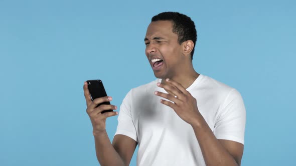 Young African Man Reacting To Loss and Using Smartphone