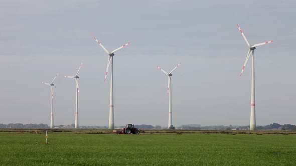 A tractor ploughing a field, with wind turbines towering over it.  East Fresia, Lower Saxony. German