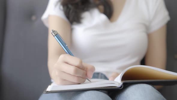 Closeup asian woman relax lying on sofa writing book and diary on sofa at home.