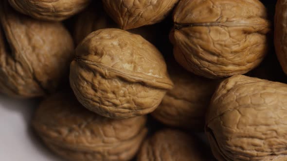 Cinematic, rotating shot of walnuts in their shells on a white surface 