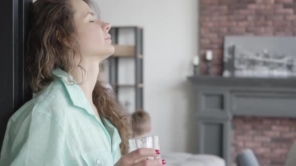 Portrait Tired Young Mother Trying To Calm Herself Standing Near the Wall with Glass of Water While