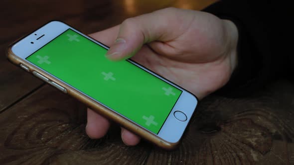 A Man a Cafe at the Wooden Table Uses the Phone with Green Screen