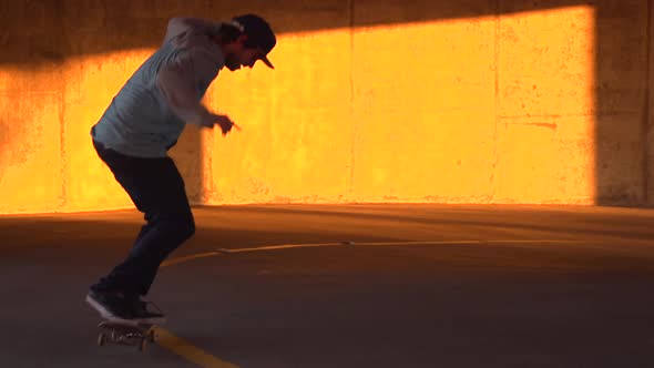 Silhouette of a young man skateboarding in a parking garage at sunset.