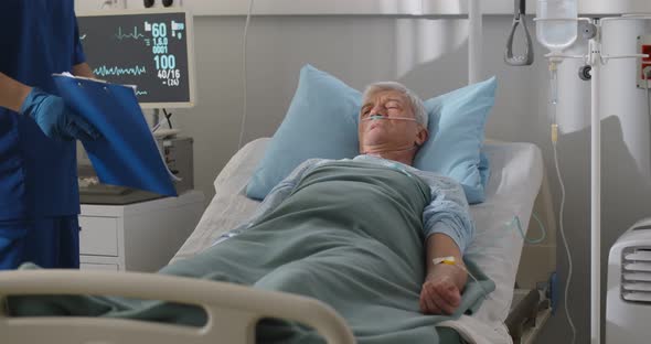 Sick Senior Man Lying in Hospital Bed and Signing Informed Consent