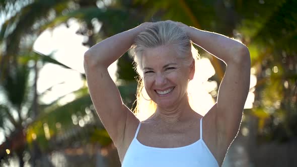 Closeup slow motion of backlit mature woman gathering her long hair and holding it behind her head a