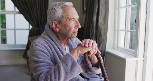 Sad senior caucasian man wearing bathrobe sitting by window