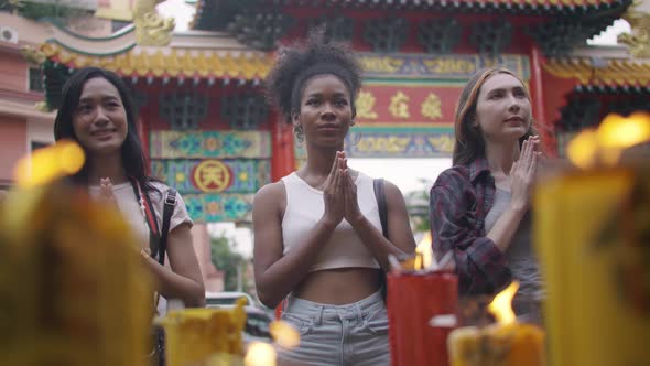 A group of multi-ethnic female friends praying at a Chinese shrine in Bangkok, Thailand.