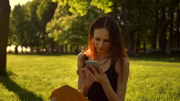 Happy Smiling Young Woman Enjoying Nature and Sunrise. Sitting on Bench in Green Summer Park Using