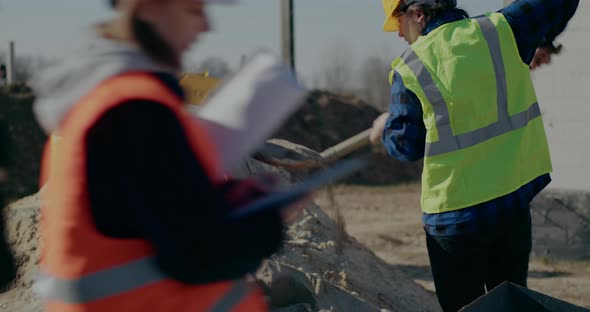 Construction Worker Putting Cement in Mixer with Shovel