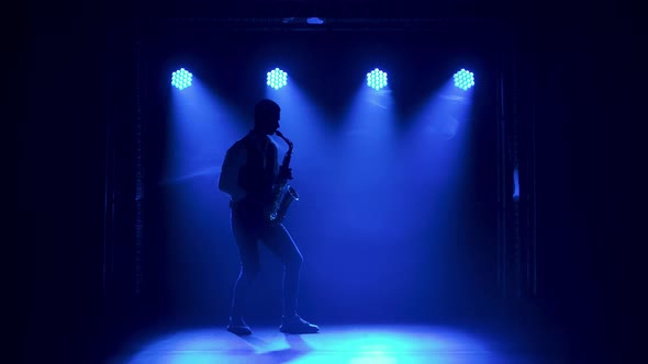 Silhouette a Young Stylish Guy Plays the Golden Shiny Saxophone in the Multicolored Spotlights on