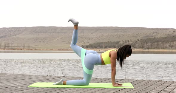 Motivated black woman doing exercises for legs with rubber stripe.