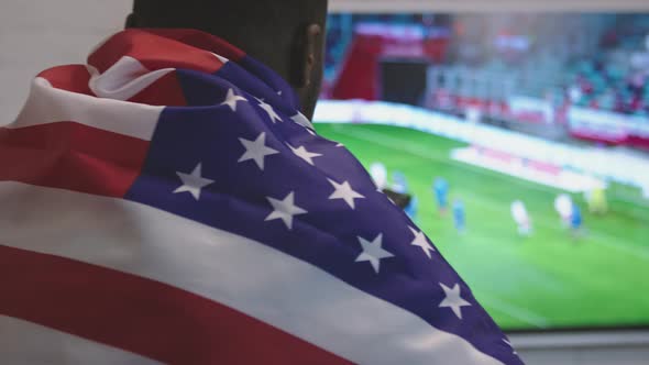 Black Man with American Flag Over the Shoulders Watching Football Game on Smart Tv