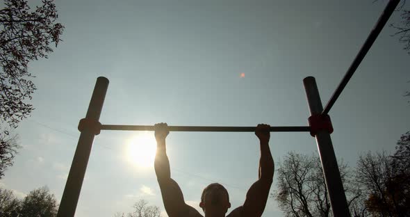 Young Man Is Doing Pull Ups on the Bar in Good Weather 