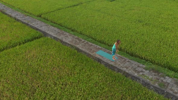Aerial Slowmotion Shot of a Young Woman Practicing Yoga on a Beautiful Rice Field