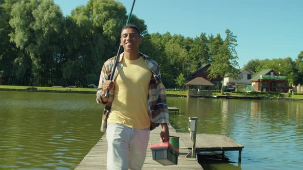 Happy Black Fisherman with Fishing Rod and Tackle Box Going for Angling on Pond