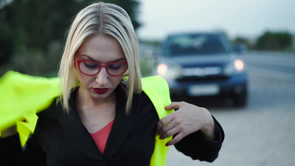 Lady Wears Reflective Safety Vest and Looks Into Camera at Broken Car at Road