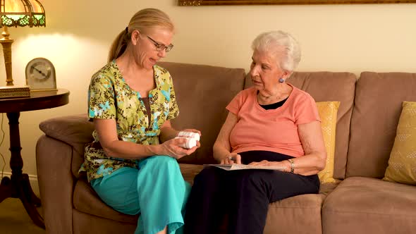 Home healthcare nurse going over medications with elderly woman while sitting in living room.