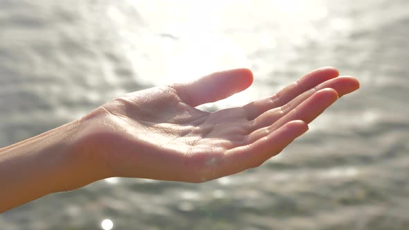 Female Cupped Hand Catches Falling Water Drops on Seascape Background