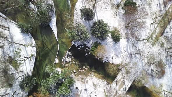 Aerial top shot over a snowy part of a park with a river and walking people, straight from above at