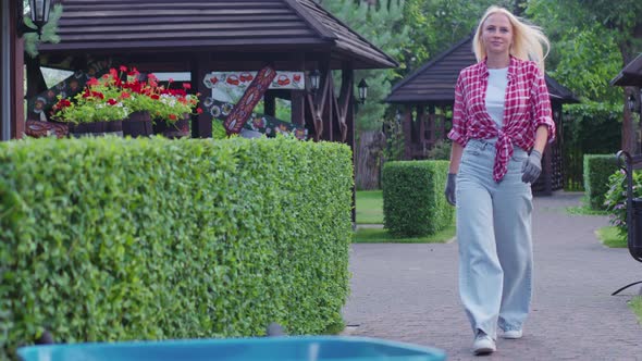 Attractive Young Woman in Jeans Approaching to Wheelbarrow on Backyard