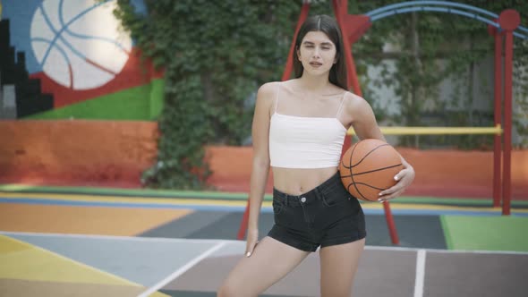 Charming Brunette Sportswoman Posing with Orange Basketball Ball on Outdoor Court