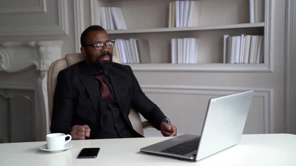 African-American Man in a Black Suit, Shirt, Stylish Glasses. A Businessman Is Working on a Desktop