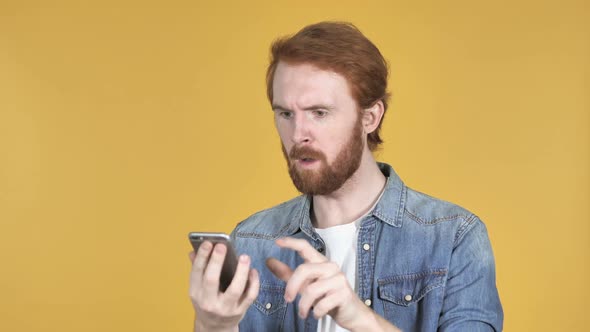 Upset Redhead Man Feeling Desperate While Using Phone Yellow Background