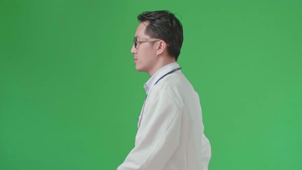 Side View Of Asian Doctor With Stethoscope Wearing Glasses And White Coat Walking On Green Screen