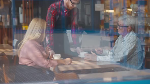 View Throguh Window of Waiter Taking Empty Cups From Table with Senior Couple