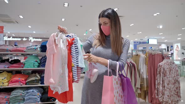 Pregnant Woman in Mask Choosing Baby Clothing