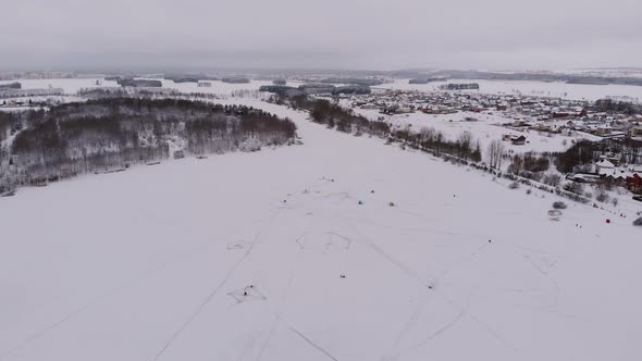 Aerial View of Frozen Lake Surrounded By Forest and Cottage Village