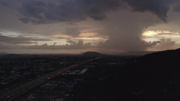 Aerial shot of a highway leading to a hill with heavy clouds on the horizon