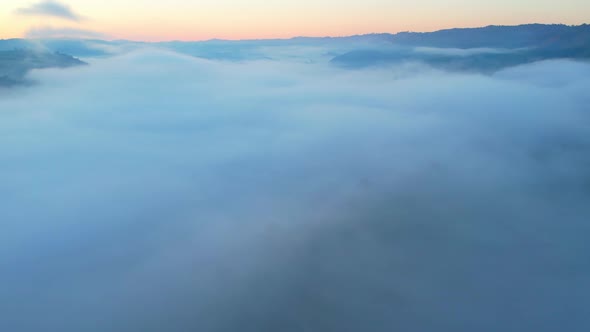 4K aerial view over mountain at sunrise in heavy fog. golden morning sunlight