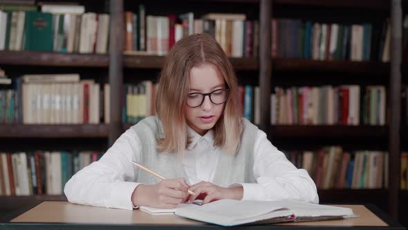 Schoolgirl Taking Notes From a Book at Library