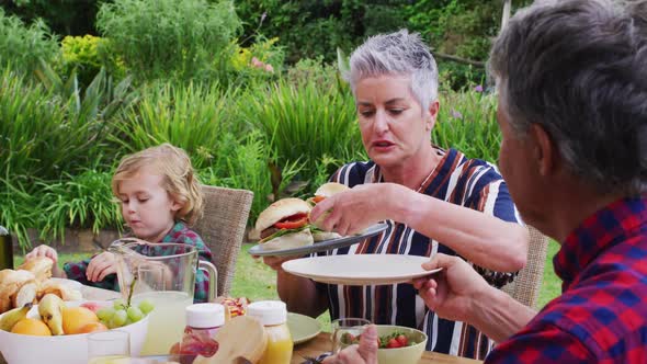 Smiling caucasian senior woman serving family having celebration meal together in garden