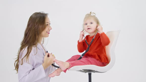 Little Toddler Sits on Chair Trying to Check Doctor's Breath with Stethoscope