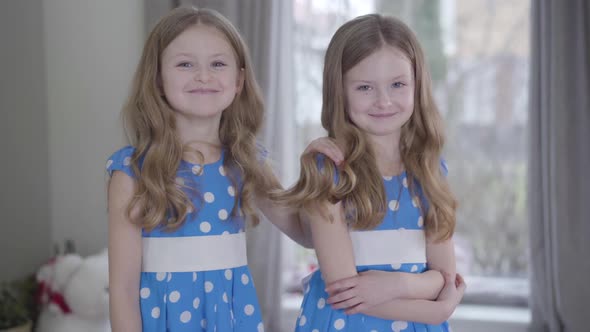 Smiling Brunette Caucasian Twin Sisters in Similar Dotted Blue Dresses Posing at Home. Positive