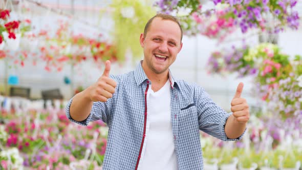 A Very Happy Lucky Man Stands in a Greenhouse and Shows Thump Up with Both Hands