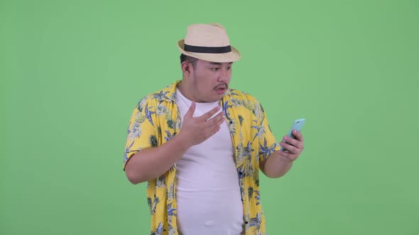 Happy Young Overweight Asian Tourist Man Using Phone and Looking Surprised